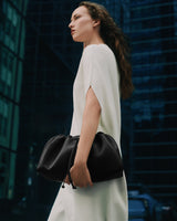 Person in a dress holding a gathered bag, standing outdoors near tall buildings.
