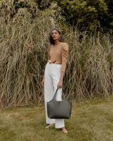 Woman standing in front of tall grass with a handbag.
