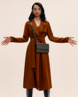 Woman in long coat with belt bag and croc-embossed leather boots, arms slightly raised