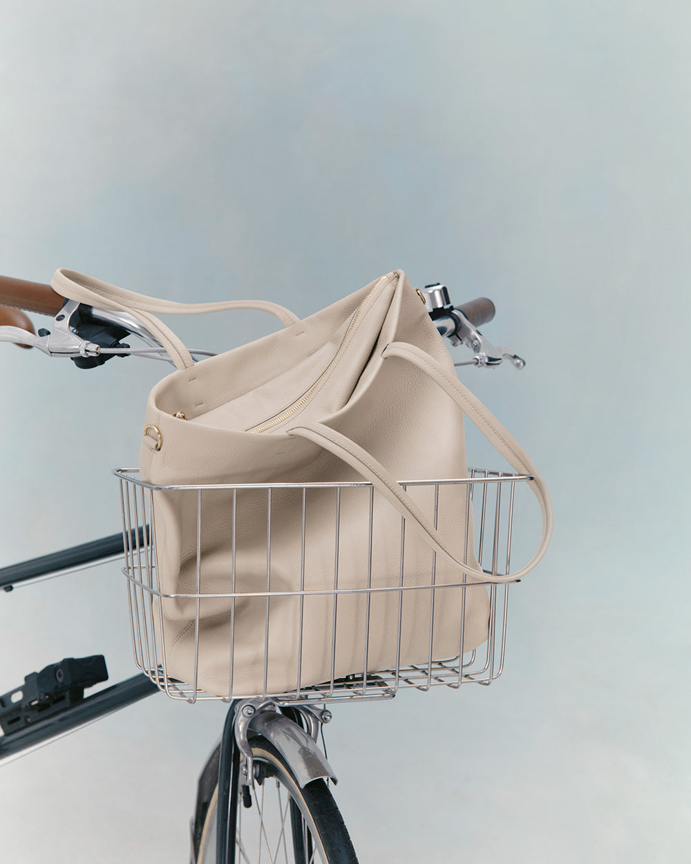 Bicycle with a bag in the front basket against a plain background.