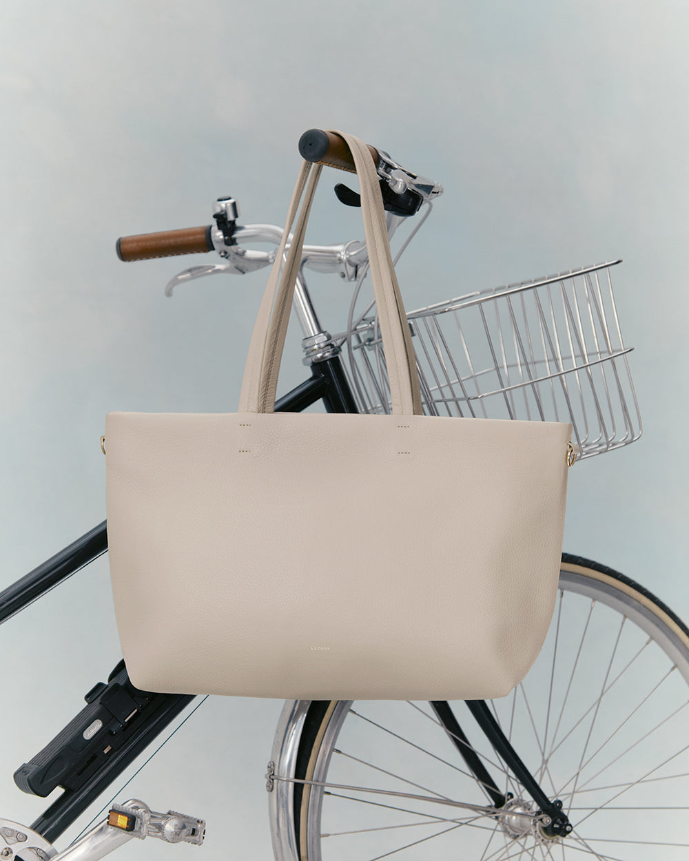 Handbag hanging on a bicycle handlebar with a basket attached.