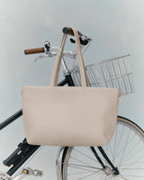 Handbag hanging on a bicycle handlebar with a basket attached.