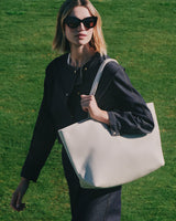 Person wearing sunglasses carrying a large tote bag walking on grass.