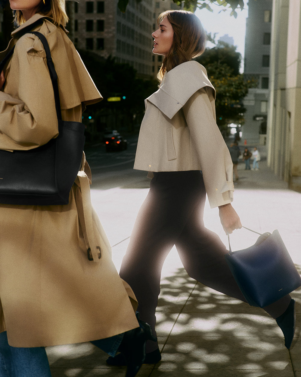 Two people walking on a city sidewalk carrying handbags.