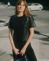 Person standing on a city street holding a bag.