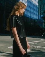 Person standing on city street holding small bag.