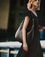 Person in a dress holding a shoulder bag outdoors.