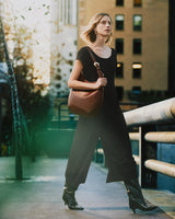 Person in jumpsuit walking in city, holding a large shoulder bag.