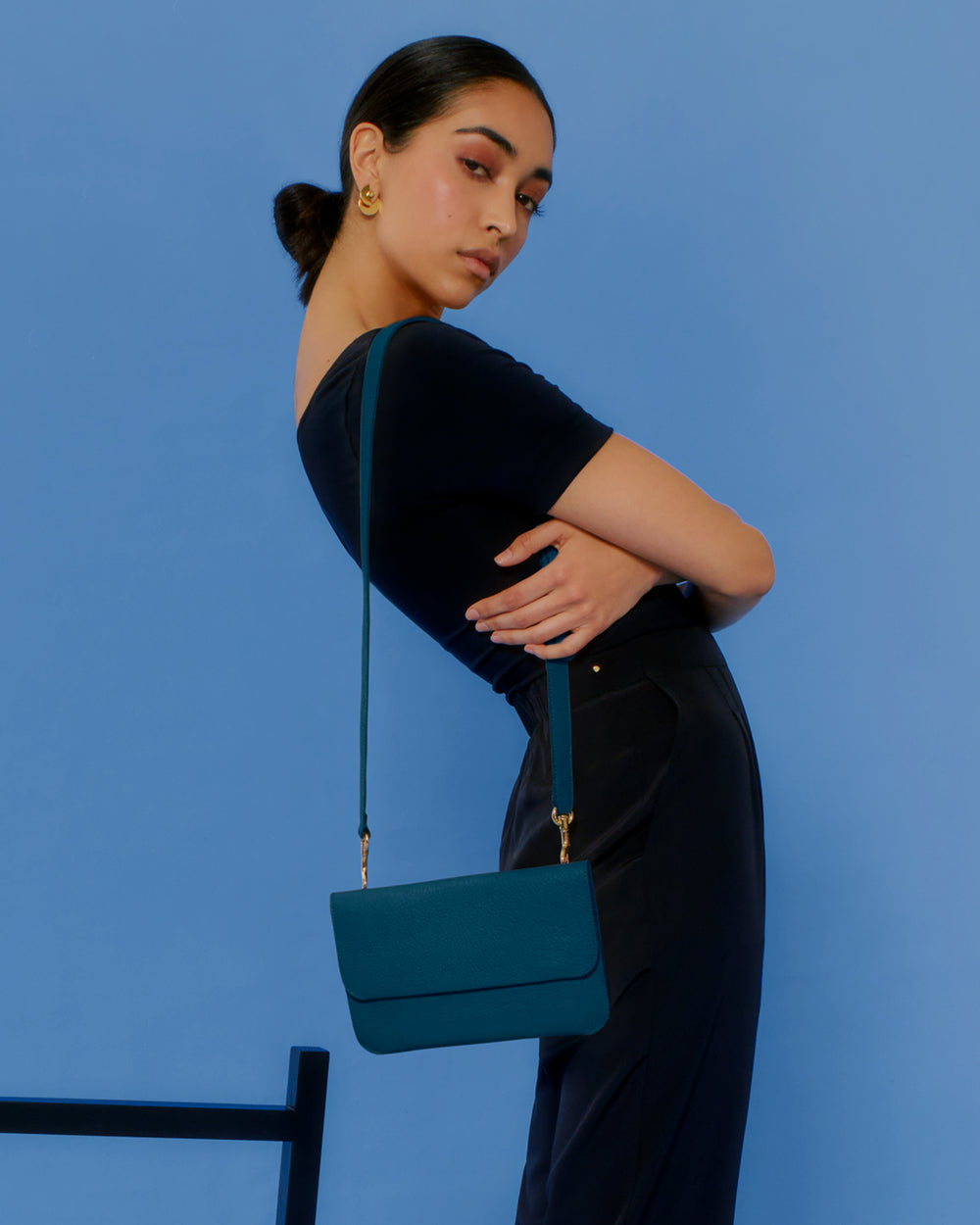 Person posing with a small shoulder bag against a plain background.