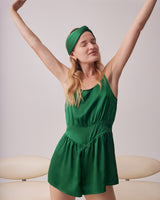 Woman stretching arms in a romper and headband, standing indoors.