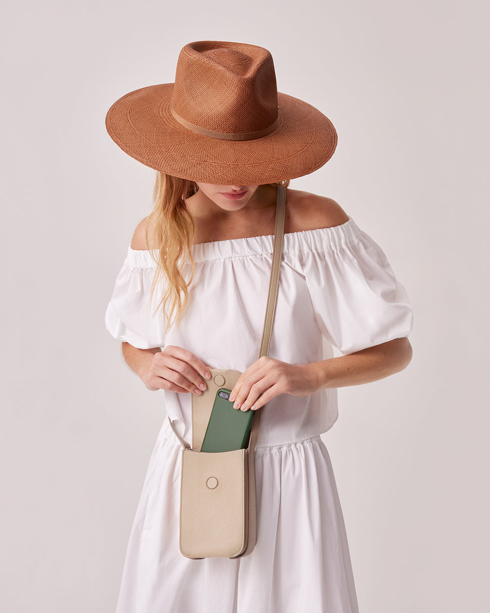 Woman in a hat and off-shoulder dress holding a purse.