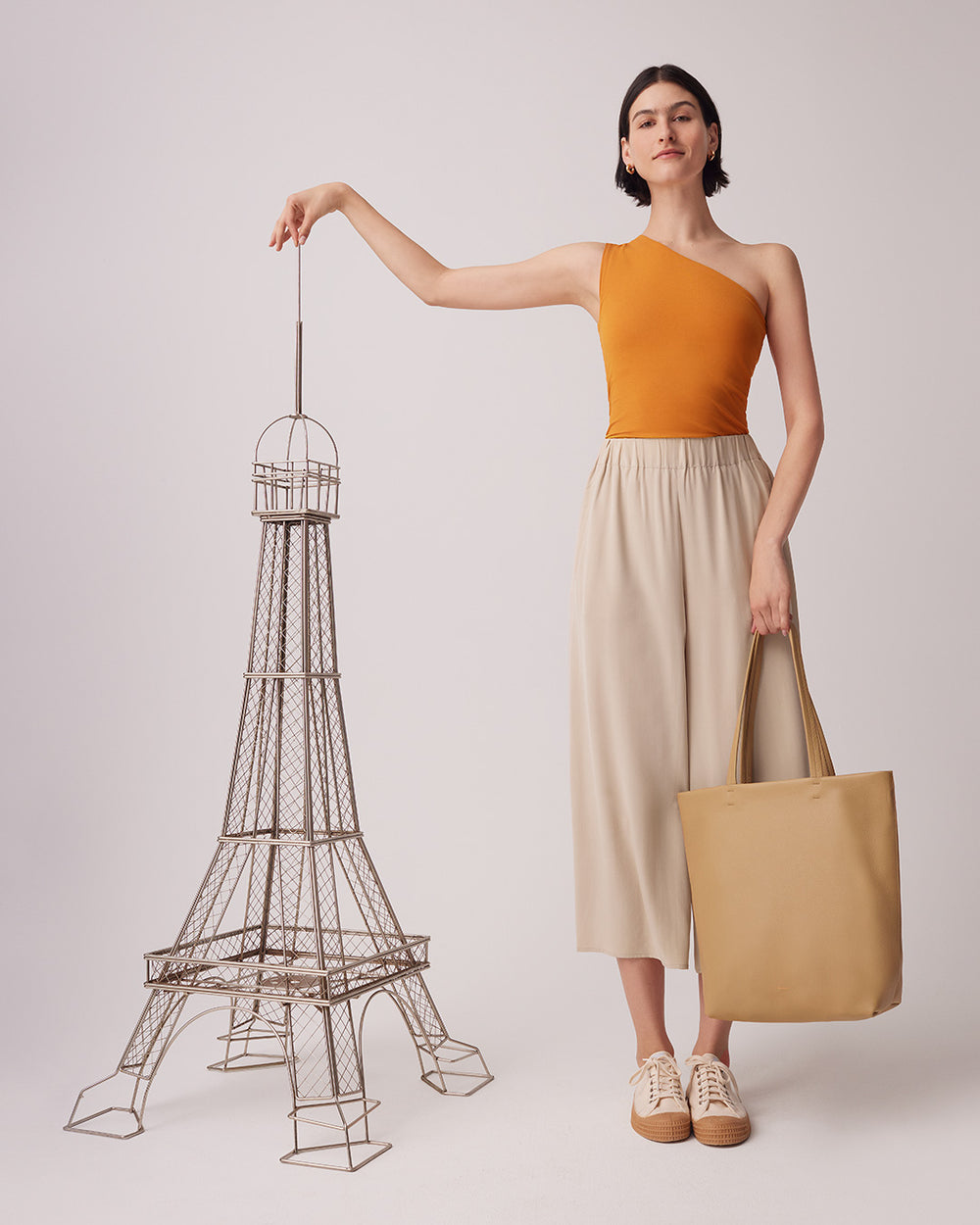 Woman standing next to a wireframe Eiffel Tower model, holding a tote bag.