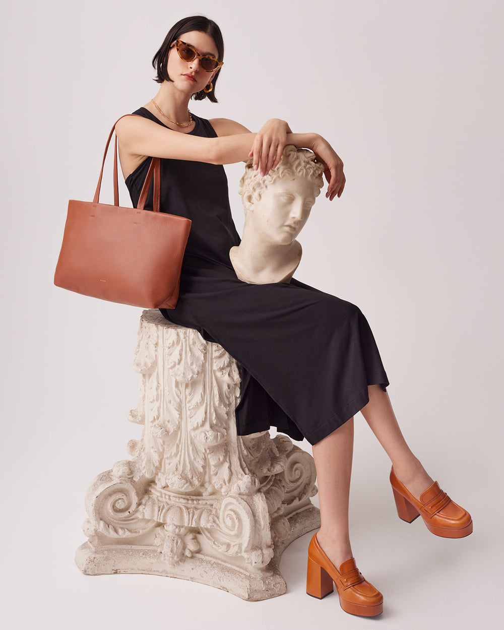 Woman sitting on a sculpture, holding a handbag, wearing sunglasses.