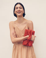 Smiling person in a dress holding a clutch with a bow detail.
