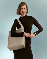 Woman standing with hand on hip and carrying a shoulder bag.
