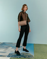 Woman standing with a crossbody bag, wearing a blouse and trousers.