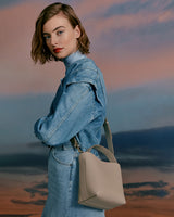 Woman standing with bag on her shoulder, looking over her shoulder.