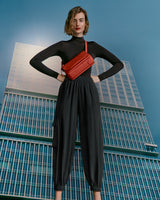 Woman standing confidently with a handbag, in front of a tall building.