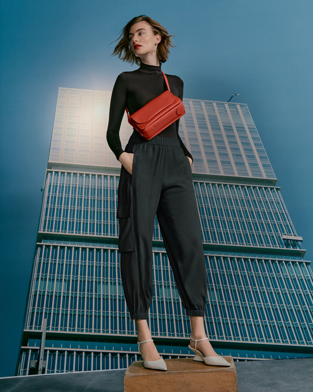 Woman standing on wooden block in front of a building backdrop.