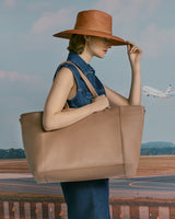 Model with large tote bag standing near an airport runway with a plane in the background