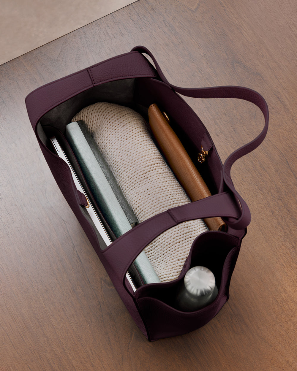 Open tote bag with bottle, books, and a rolled blanket inside on a table