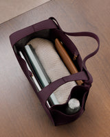 Open tote bag with bottle, books, and a rolled blanket inside on a table