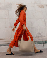 Woman walking with a bag against a wall background.