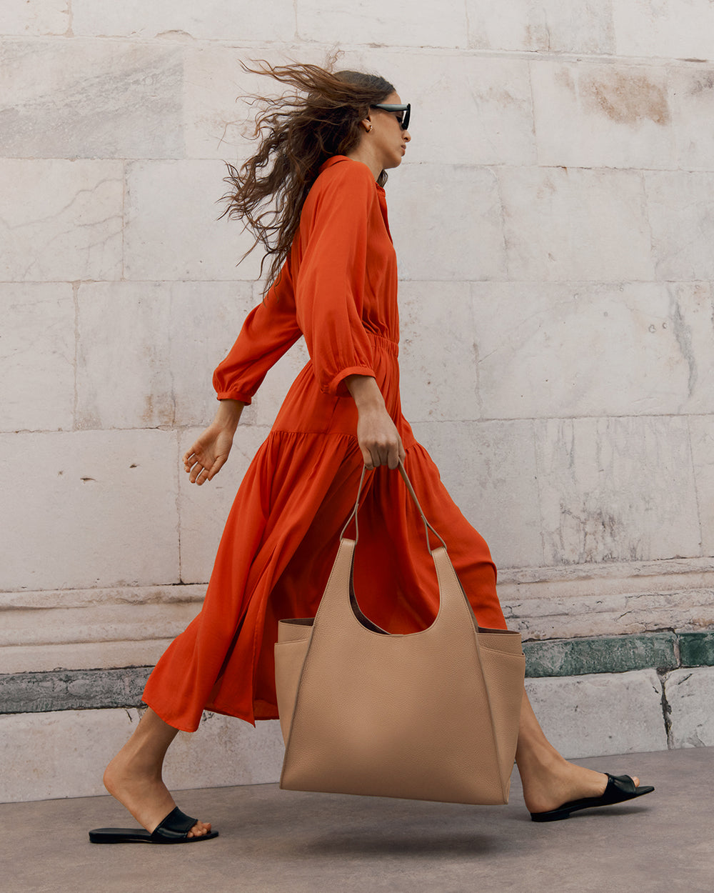 Woman walking briskly with a handbag and sunglasses.