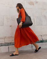 Woman walking with a large bag, wearing a dress and sunglasses.