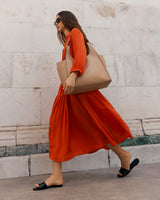 Woman walking with a tote bag and wearing a dress and sandals.