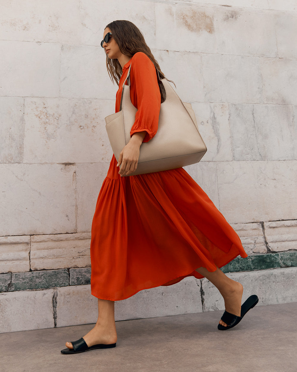 Woman walking with a tote bag wearing a dress and sandals.