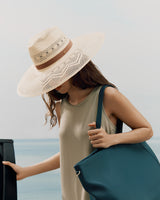 Woman in a hat and sleeveless top, carrying a large bag, opens a door.