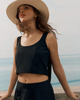 Person wearing a sleeveless top and wide-brimmed hat, standing outdoors near the ocean.
