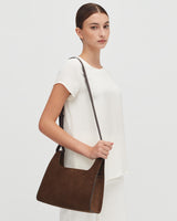 Woman standing with a shoulder bag and a short-sleeved top.