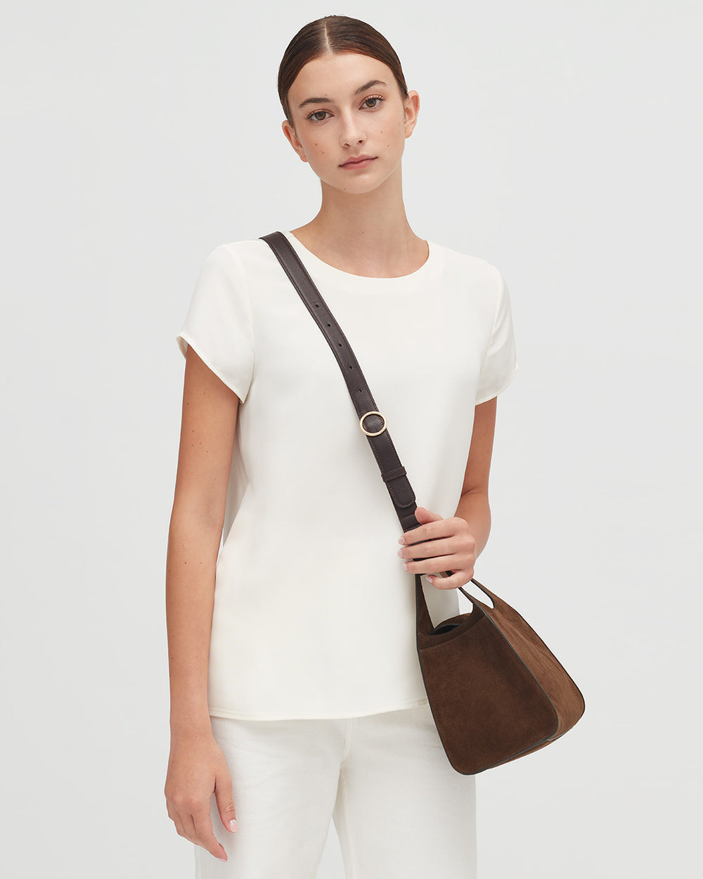 Woman standing with a shoulder bag and wearing a T-shirt.