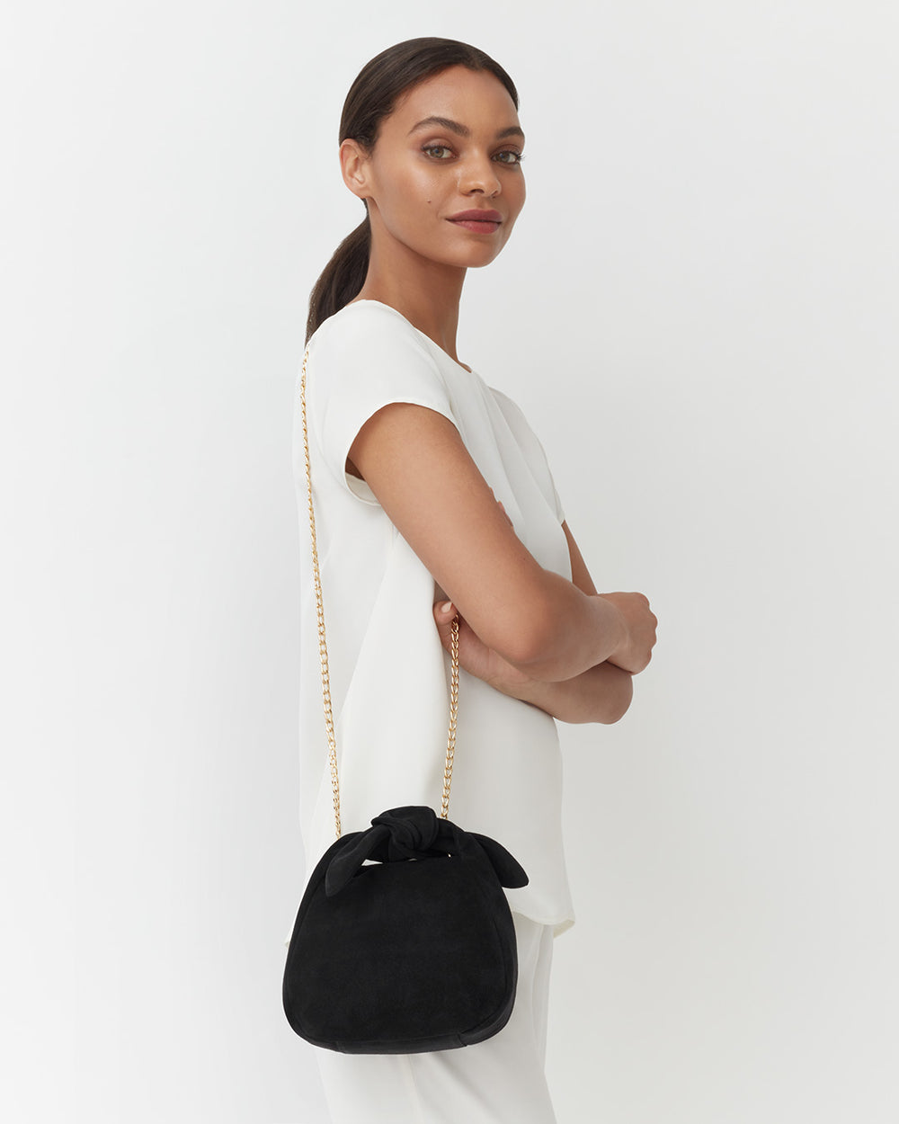 Woman standing, looking over her shoulder, holding a handbag with chain.