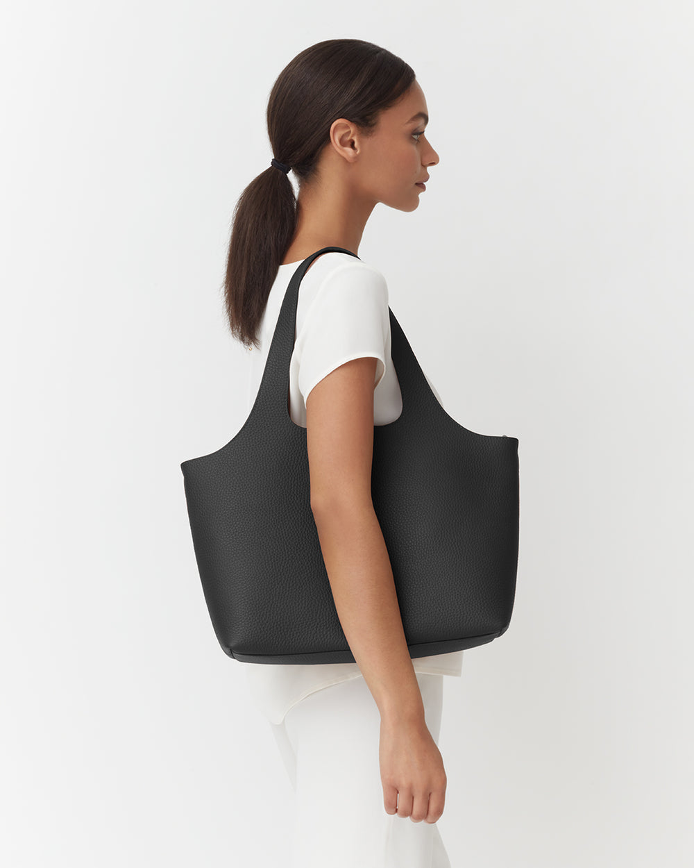 Woman with ponytail carrying a large tote bag on her shoulder, facing away.