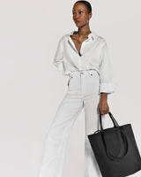 Woman standing with a handbag, wearing a buttoned shirt and pants.