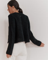 Woman viewed from behind, wearing a sweater and white pants.