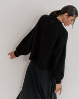 Woman in sweater walking against a wall, looking down.