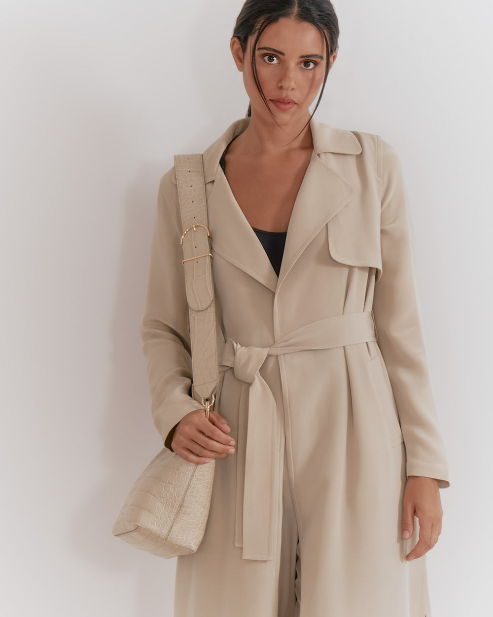 Woman in a trench coat holding a bag and wearing earphones.