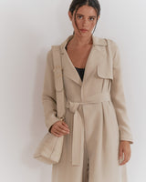 Woman in a trench coat holding a bag and wearing earphones.