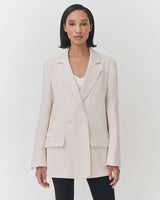 Woman standing and looking at the camera, wearing a blazer and a top.