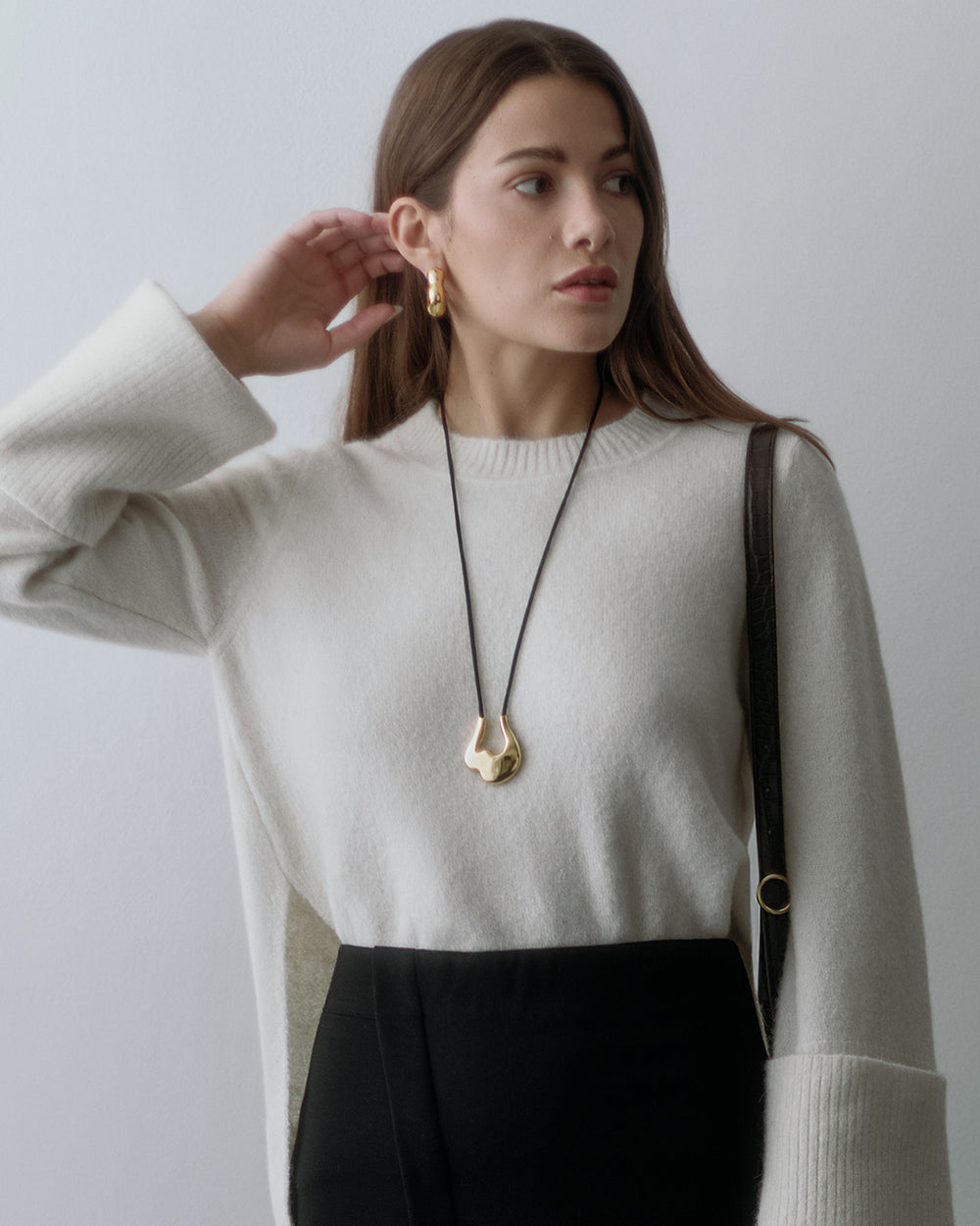 Woman in sweater and pants with long pendant necklace and shoulder bag