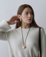 Person wearing a sweater, long necklace, and earrings, holding a strap over their shoulder.