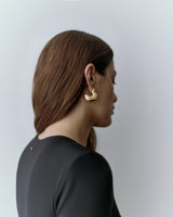 Person wearing golden earrings, viewed from the side, with a smooth fabric top