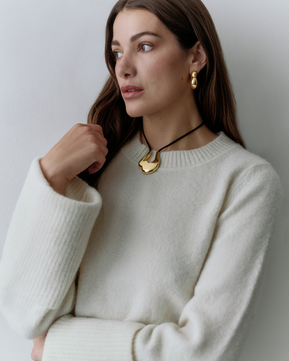 Woman wearing long-sleeve sweater, necklace, and drop earrings gazing to her right