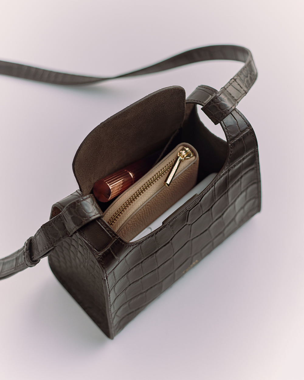 Crossbody bag with croc-embossed leather, containing a zipper pouch and a lipstick.