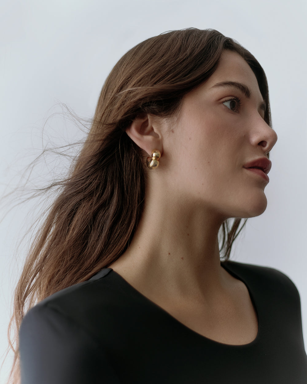 Person wearing a top and gold hoop earrings, looking to the side