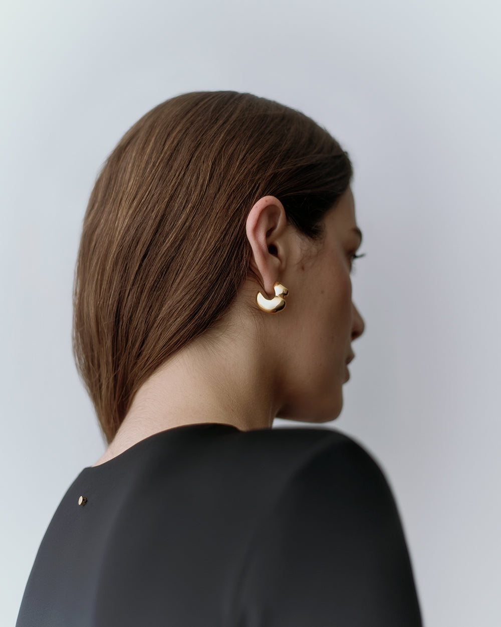 Person wearing a black top and gold earrings looking to the side